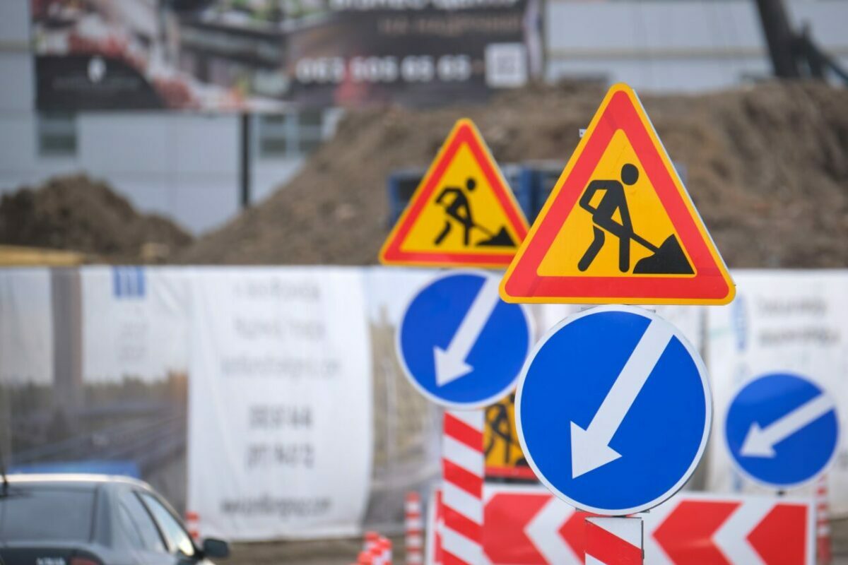 Roadworks warning traffic signs of construction work on city street and slowly moving cars